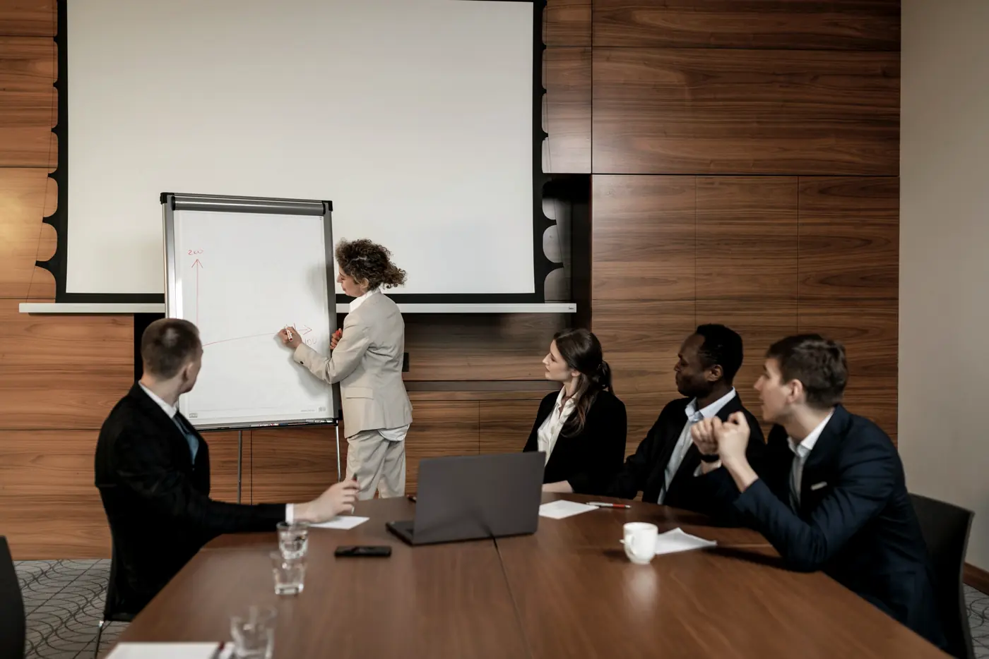 A colleague briefing a seated team from a flip chart in a panelled meeting room.